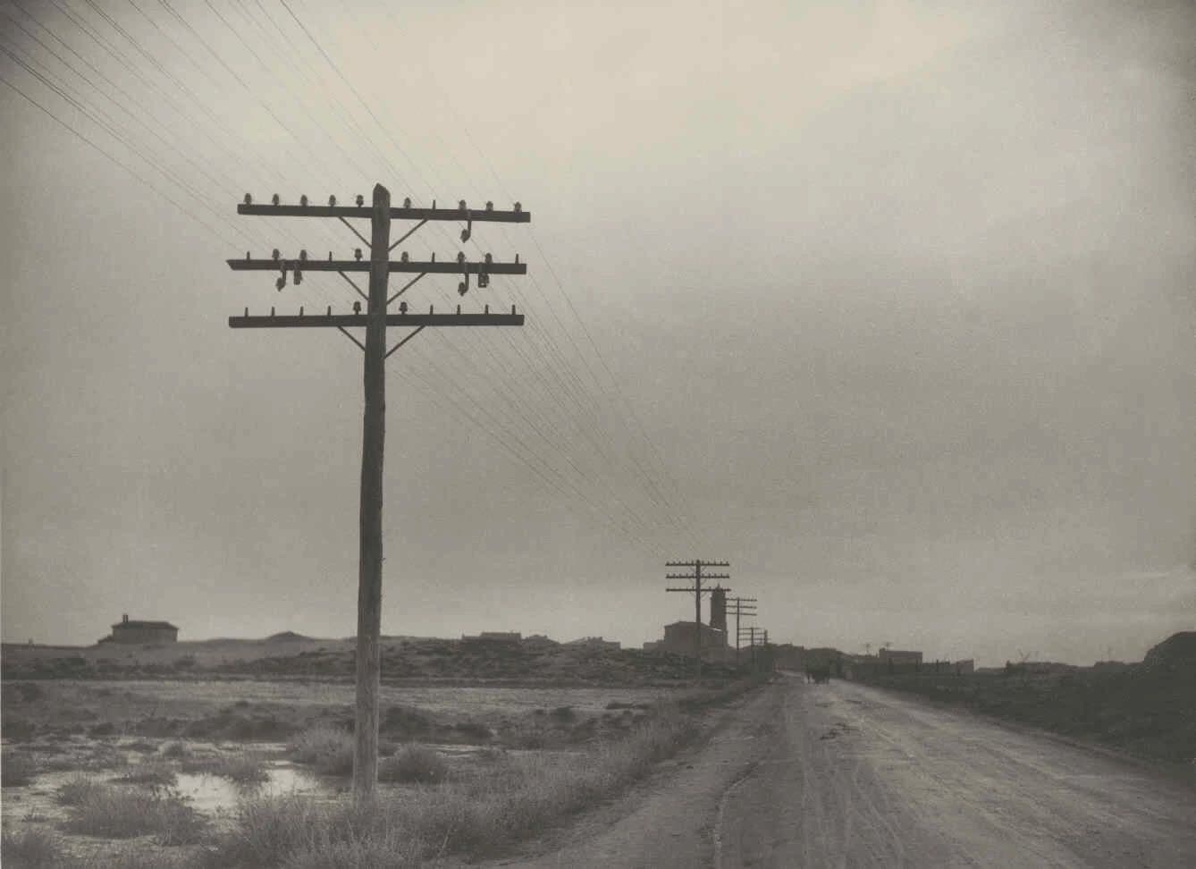 An old photograph of a dirt road in the countryside, lined with wooden telephone poles