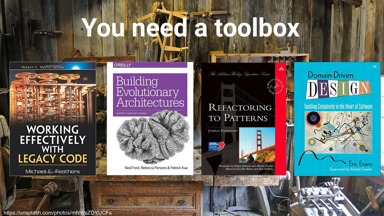 A workshop full of old tools, with the covers of Working Effectively with Legacy Code, Building Evolutionary Architectures, Refactoring to Patterns and Domain-Driven Design