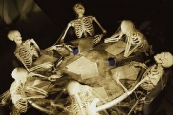 Skeletons sitting around a meeting table covered in papers