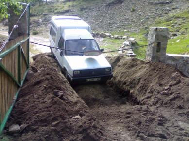 A white van in a freshly dug trench beside a gate, with the chain across the track still in place