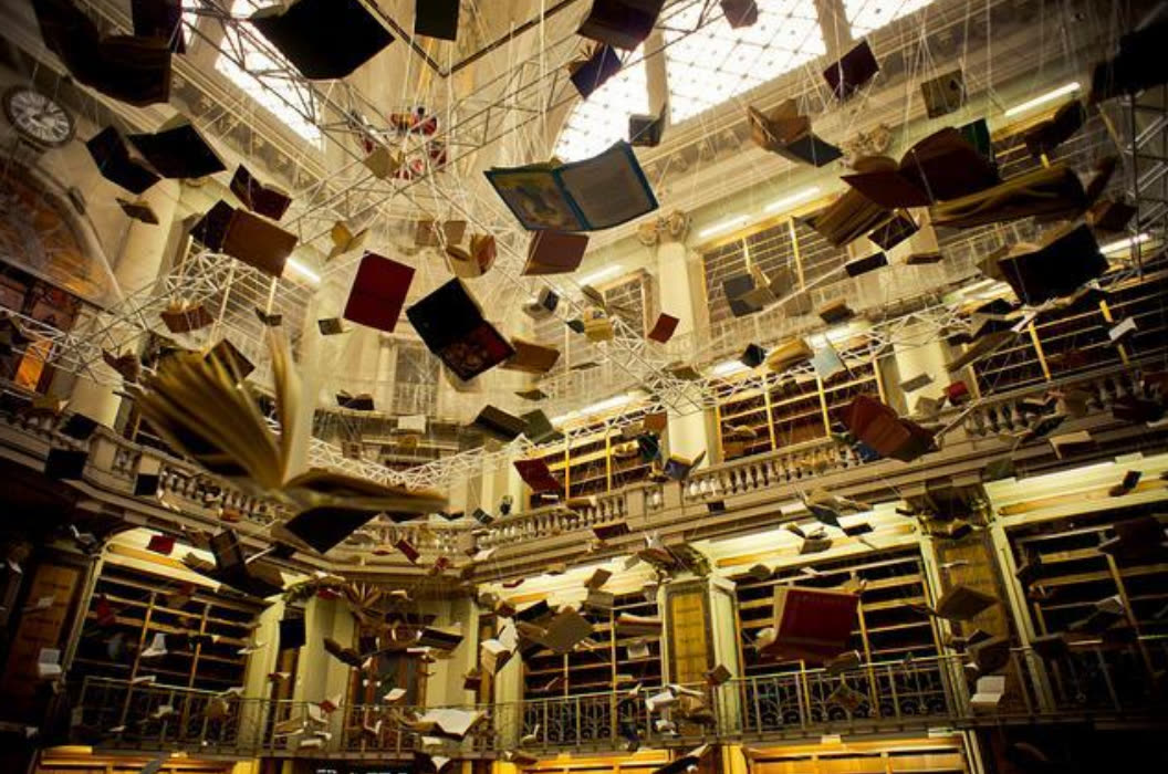 Hundreds of open books hanging in mid-air inside a grand old library