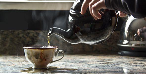 A hand pouring tea from a teapot into a small cup
